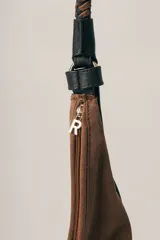 Cartera tipo hobo de gamuza color marrón, con correa trenzada de cuero negro y detalles laterales en cuero negro.