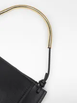 Mini cartera de piel vacuna color negro, con solapa frontal y cierre de cremallera. Cuenta con un asa de mano que combina cuero y una pieza metálica tubular dorada, y lleva el logo grabado en la parte frontal.