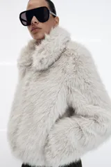Abrigo corto de piel sintética en color beige, con cuello solapa, manga larga y cierre frontal con cremallera. Incluye bolsillos laterales y forro interior a tono.