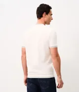 Remera de manga corta y cuello redondo color blanco crudo, con detalles de ribetes oscuros en cuello, mangas y ruedo, y un pequeño escudo bordado en el pecho.