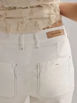 Pantalón tipo cigarette de lino color mostaza, con pinzas en la pierna trasera y dobladillo visible con costura contrastante.