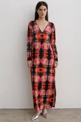 Vestido largo de corte recto con escote en V y mangas largas. Presenta un estampado abstracto en tonos rojos, naranjas y negros, con tajos laterales en el ruedo.