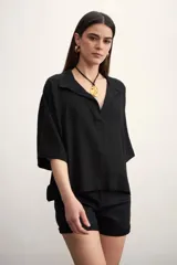 Blusa negra de corte holgado con cuello polo y cierre frontal parcial. Presenta mangas cortas amplias y un diseño minimalista.