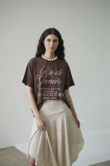 Remera de algodón color marrón con estampado frontal en rosa que dice "Rio de Janeiro Captivate Journey Copacabana Lucha Clothing since 2019".