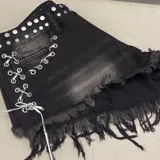 Short de denim negro con efecto lavado, tachas metálicas en la pretina, cordones cruzados con ojalillos y dobladillo desmechado con flecos.