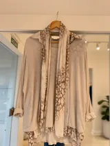 Sweater de punto ligero en color beige, con diseño de capas que incluye una bufanda integrada con estampado animal print en tonos tierra. Presenta mangas largas con puños vueltos y un corte holgado.