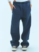 Pantalón de jean azul de corte babucha, tiro medio, con elástico en la cintura, bolsillos delanteros y logo bordado en amarillo en la pierna derecha.