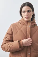 Campera puffer negra con diseño acolchado, capucha integrada y cierre frontal con botones a presión. Presenta puños elásticos y costuras decorativas en el frente.