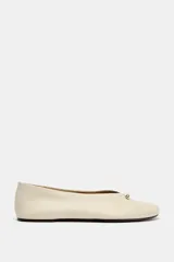 Zapato plano tipo bailarina en piel color beige, con efecto soft y pespuntes en la parte frontal. Presenta escote en pico con detalle metálico y acabado en punta redonda.