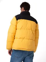 Campera puffer Caterpillar color amarillo y negro, con cuello alto, cierre frontal y bolsillos con cremallera. Presenta el logo de la marca estampado en el pecho.