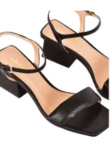 Sandalias de cuero negro texturizado, con tira ancha sobre los dedos, pulsera ajustable al tobillo y tacón geométrico de 6 cm.