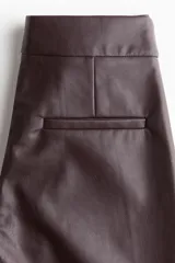 Pantalón de tejido revestido color marrón oscuro, de corte recto y tiro alto, con pretina prolongada y cierre frontal.