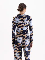 Remera de manga larga con cuello polo y cierre frontal parcial. Presenta un diseño estampado que combina rayas horizontales en tonos azul marino y tostado con un motivo floral en celeste.