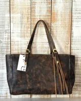 Cartera tipo tote de cuero con acabado envejecido en tonos marrón y negro, con doble asa de hombro, hebillas decorativas metálicas y detalle de flecos colgantes.