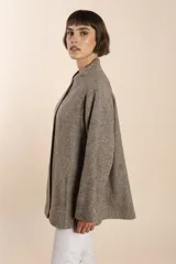 Capa de lana fina sin teñir, con estampado de espiga en tonos marrones y beige. Presenta cuello alto, mangas amplias, bolsillos laterales y pinzas en la parte delantera.