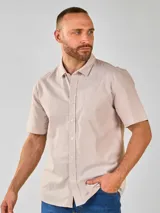 Camisa de manga corta con cuello camisero y botones frontales. El tejido es de color crema con un patrón de cuadros pequeños en negro y marrón.