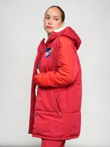 Parka larga de abrigo Umbro del Club Nacional de Football, color rojo con detalles en naranja en las mangas. Cuenta con capucha, cierre frontal con botones a presión y escudo del club bordado en el pecho.
