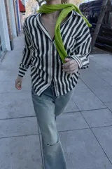 Camisa de cuello solapa con escote pico y manga larga. Presenta un bolsillo delantero de plastrón y bajo con aberturas laterales con cordones ajustables. Cierre frontal con botones.