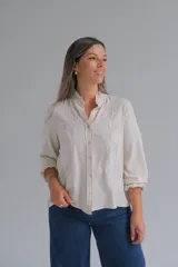 Blusa de lino color beige con cuello mao y detalles de volados sutiles. Presenta bordados florales en color blanco en el frente y mangas largas con puños elásticos.