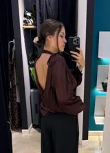 Blusa de satén color marrón chocolate, con diseño de espalda descubierta, cuello alto y mangas largas abullonadas.