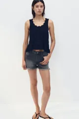 Musculosa corta negra de punto crochet con escote redondo pronunciado con ribete festoneado y bajo acanalado de volado. Sin mangas.