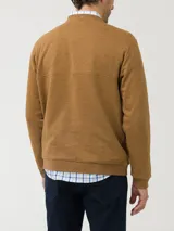 Buzo de algodón orgánico color naranja tostado, con cuello redondo y apertura frontal con broches a presión. Presenta un bolsillo pequeño en el pecho con parche decorativo y mangas largas.
