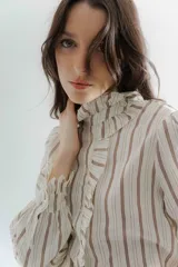 Camisa de corte clásico con estampado de rayas verticales, cuello alto con volados frontales y mangas largas con puños con volados.