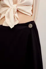 Falda larga cruzada de satén negro, con diseño irregular y gran caída con movimiento. Incluye un pin de flor con perlitas.