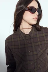 Camisa tipo leñadora de corte oversize, con estampado de cuadros en tonos negro y marrón. Presenta cuello clásico, cierre frontal con botones y mangas largas con puños abotonados.