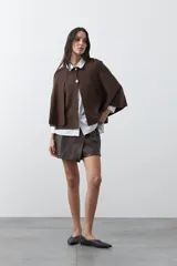 Saco tipo capa de punto color negro, con silueta fluida, corte amplio y cierre frontal con dos botones dorados.