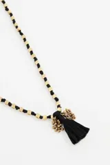 Collar largo con diseño de cuentas doradas intercaladas en un cordón negro, finalizado con una borla negra central.