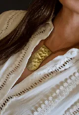 Collar con dije rectangular de bronce con textura martillada, montado sobre un cordón de cuero fino.