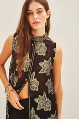 Camisa larga sin mangas, abierta al frente con cuello mao, confeccionada en tejido negro transparente con estampado floral en hilo dorado metalizado.