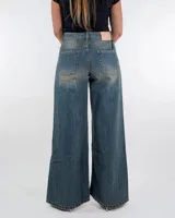 Pantalón de jean de tiro medio y corte wide leg, con diseño de cinco bolsillos y acabado desgastado vintage. Presenta costuras verticales en el frente de las piernas y ruedo desflecado.