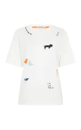 Remera blanca de algodón con cuello redondo y mangas cortas. Presenta un estampado disperso de perros de diferentes razas y colores, junto con un detalle de texto bordado cerca del cuello.