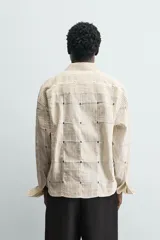 Camisa de corte relajado confeccionada en una mezcla de algodón y lino con textura semitransparente. Presenta un diseño de rayas verticales, cuello solapa, manga larga con puños abotonados y cierre frontal con botones.