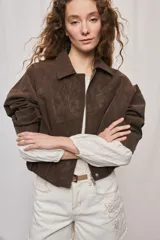 Campera marrón de poliuretano con acabado texturizado, silueta relajada, cuello camisero, cierre frontal, hombros caídos y mangas amplias con efecto abombado.