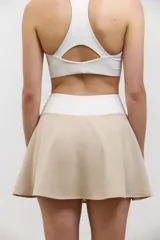 Pollera deportiva de corte acampanado color beige, con calza corta integrada de color blanco. Presenta cintura ancha de tiro alto y bolsillo invertido en la calza para guardar pelotas.