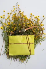 Cartera bandolera de cuero flexible color amarillo, con trenza artesanal al frente, interior forrado y correa larga con herrajes de metal.