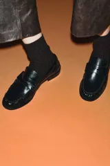 Mocasín plano negro de cuero liso, con antifaz, copete subido y detalle de fruncidos en la parte delantera. Punta redonda y suela de 2,5 cm de altura.