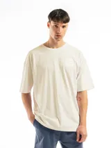 Remera oversize de algodón color blanco hueso con cuello redondo y manga corta. Presenta un pequeño estampado circular en el pecho con texto en blanco.