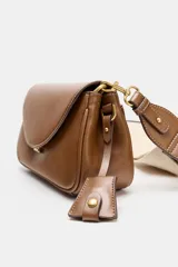 Bolso bandolera de formato alargado en color negro, con solapa frontal y cierre metálico. Incluye una correa ajustable de tejido en color crudo y herrajes dorados.