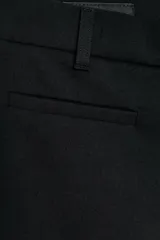 Pantalón de tiro medio con corte flare, cierre frontal con cremallera, botón interior y ganchos metálicos, con falsos bolsillos de vivo en el delantero.