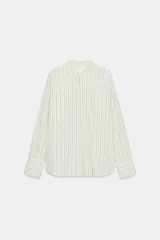 Camisa de corte oversize confeccionada en tejido con viscosa, con estampado de rayas verticales. Presenta cuello mao, cierre frontal con botones ocultos bajo solapa, mangas largas con puños anchos y bolsillos de plastrón en el delantero. El bajo es asimétrico y redondeado.