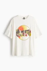 Remera de algodón de corte oversized, color blanco, con cuello redondo y mangas cortas con hombros caídos. Presenta un estampado frontal circular con el logo de la banda The Doors en tonos amarillos, naranjas y negros.