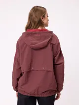 Campera rompevientos color bordó con cierre frontal, capucha con cordones ajustables y franjas laterales en tono más oscuro. Presenta puños elásticos y bolsillos frontales.