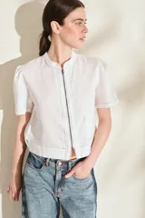 Blusa de lino color amarillo, con cuello mao, cierre frontal con cremallera y mangas cortas abullonadas. Cuenta con un bolsillo aplicado en el frente.