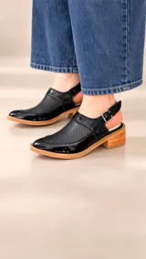 Zapatos destalonados de cuero color tostado, con perforaciones en el empeine y cierre lateral con hebilla metálica.