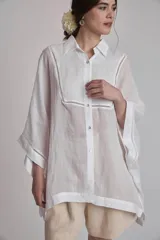 Camisa blanca de lino con cuello clásico, cierre frontal con botones, mangas anchas 3/4 y detalles de bordado calado en el canesú y los puños.