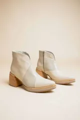 Botas cortas de cuero color crema, con puntera fina, paneles laterales con textura de piel de reptil, cierre lateral con cremallera y tacón geométrico de madera.